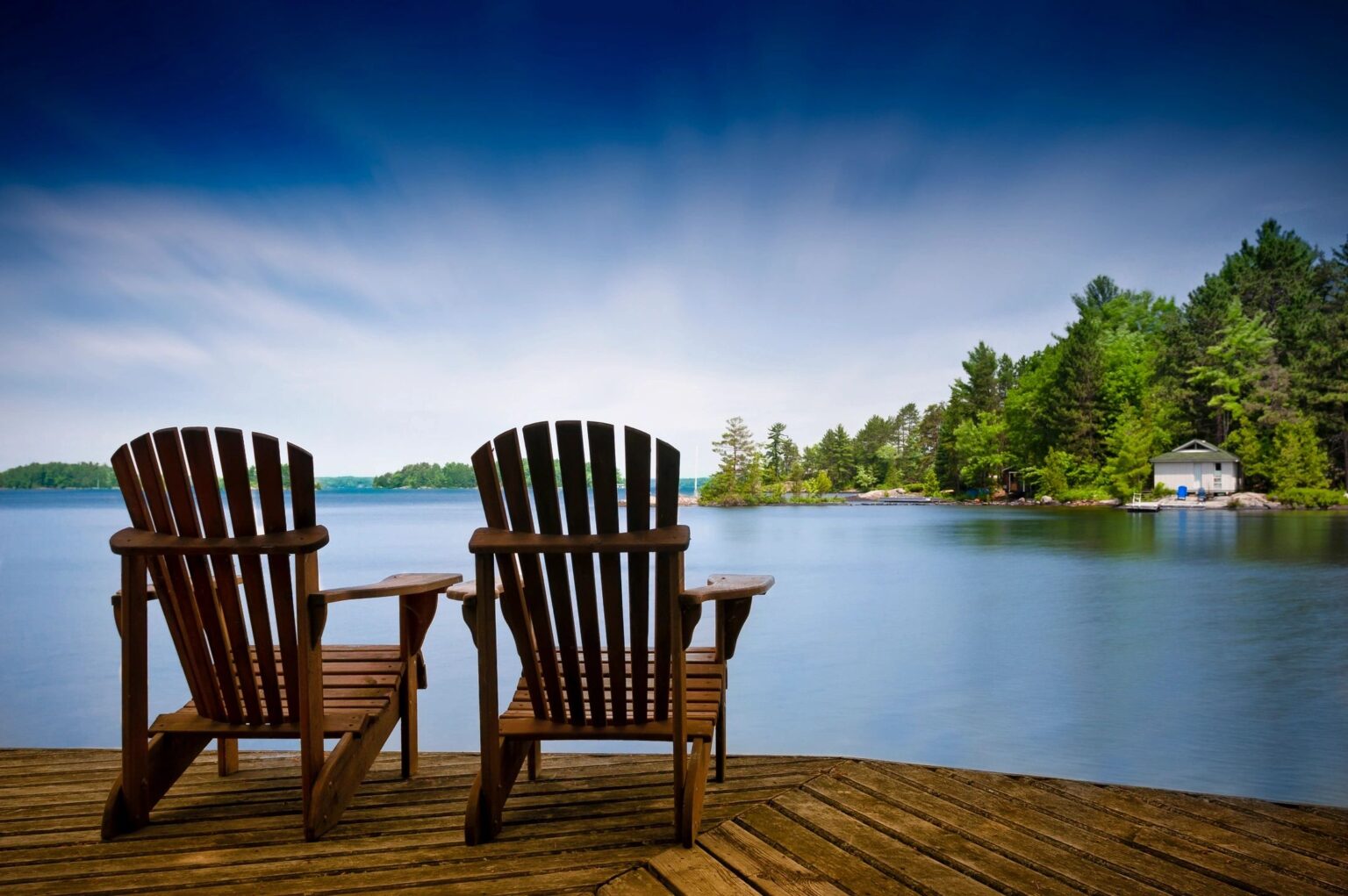 Two wooden chairs on a dock overlooking the water.